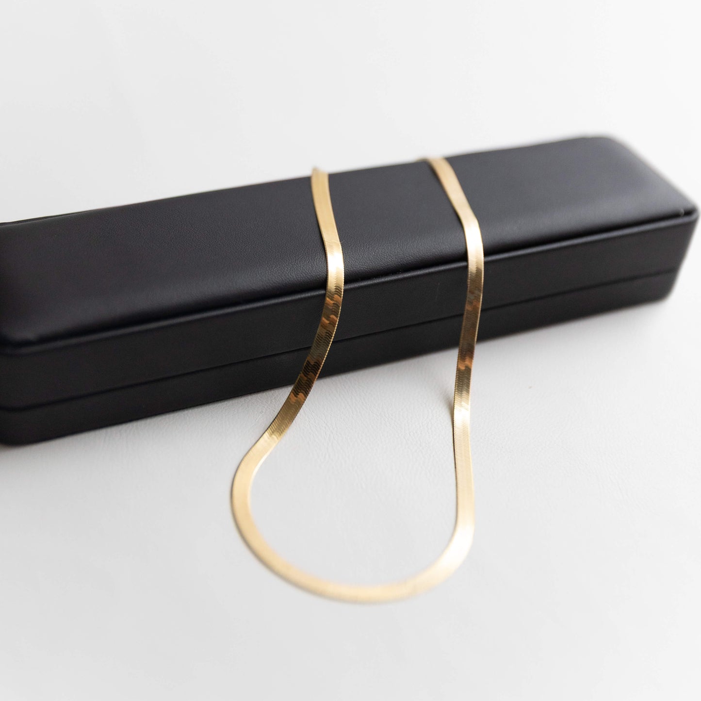 Gold herringbone necklace on a black jewelry box against a white background