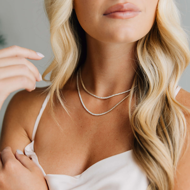 Woman wearing a 14k yellow gold tennis necklace with a neutral background