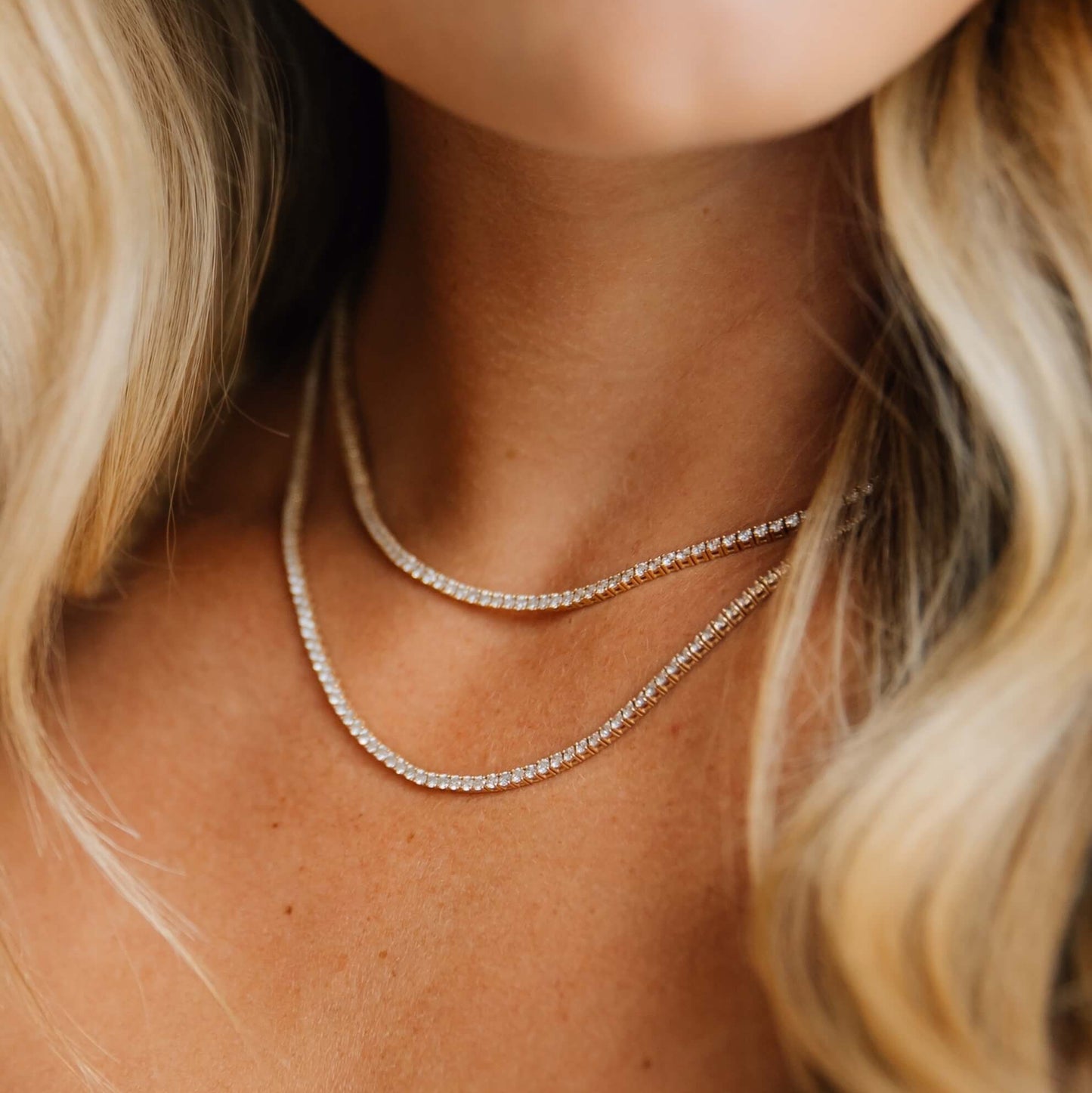 Close-up of a person wearing a 14k yellow gold tennis necklace with blonde hair.