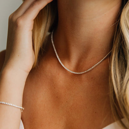 Close-up of a woman wearing a 14k yellow gold tennis necklace with a neutral background