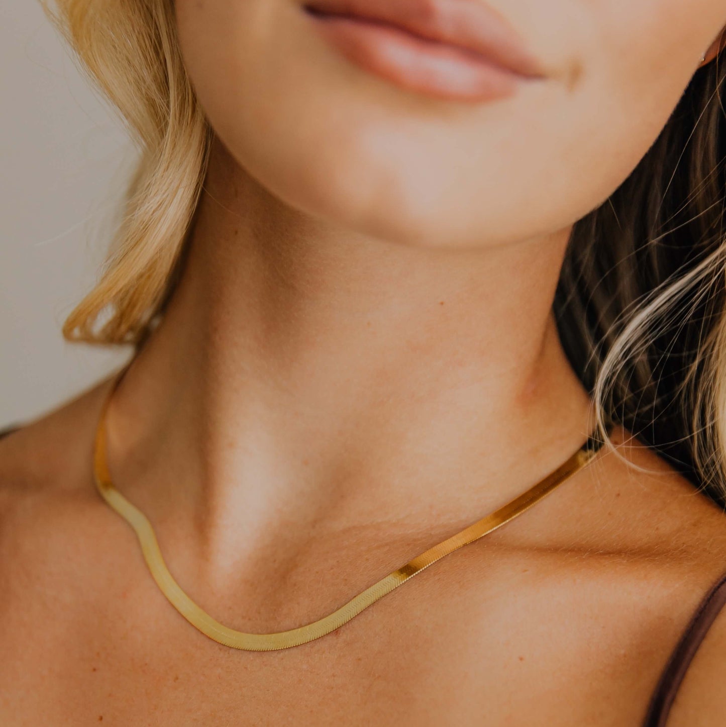 Close-up of a woman wearing a gold herringbone necklace against a neutral background