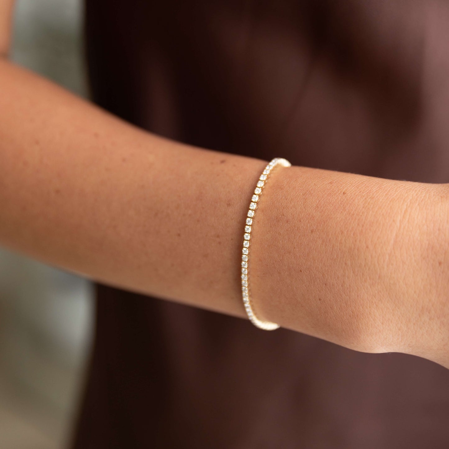 Close-up of a woman's arm wearing a 14K yellow gold diamond tennis bracelet on a blurred background