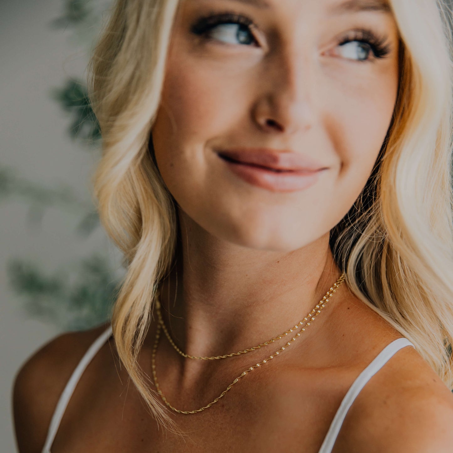 Woman wearing a white top and gold twisted herringbone necklace with a blurred background