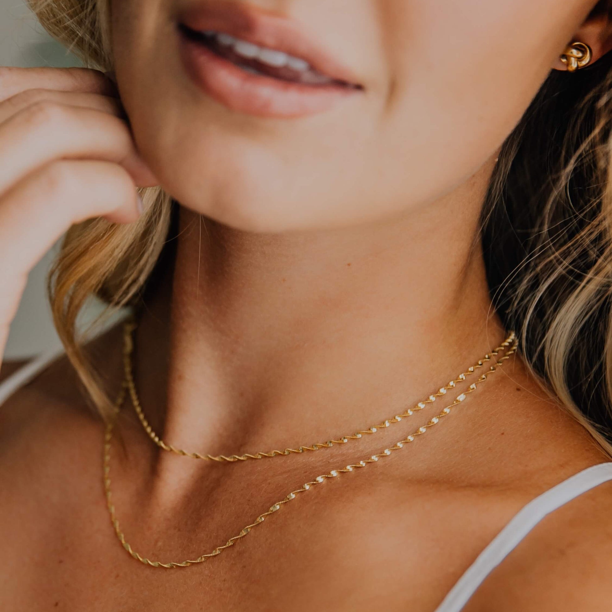 Close-up of a woman wearing two gold twisted herringbone necklaces and white top.