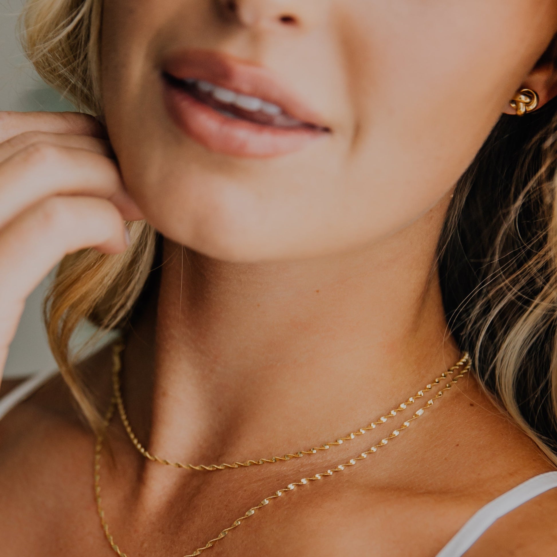 Close-up of a woman wearing a gold necklace and 14k yellow gold love knot earrings