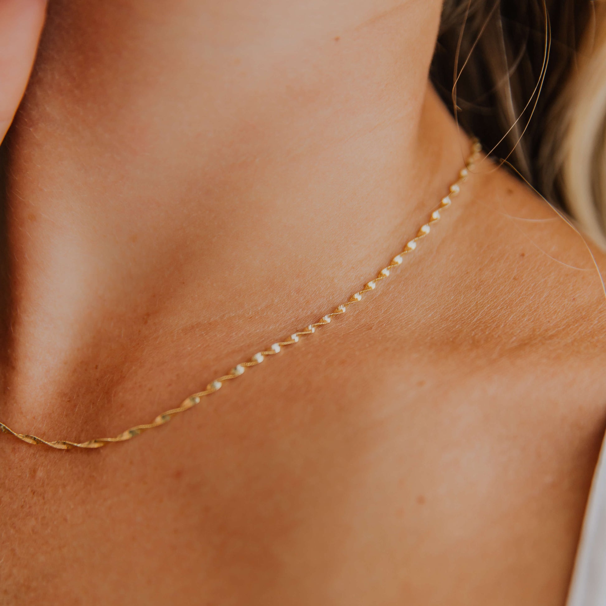 Close-up of a woman wearing a gold twisted herringbone necklace on a neutral background