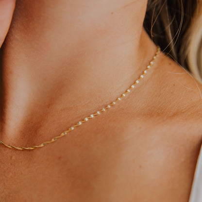 Close-up of a woman wearing a gold twisted herringbone necklace on a neutral background