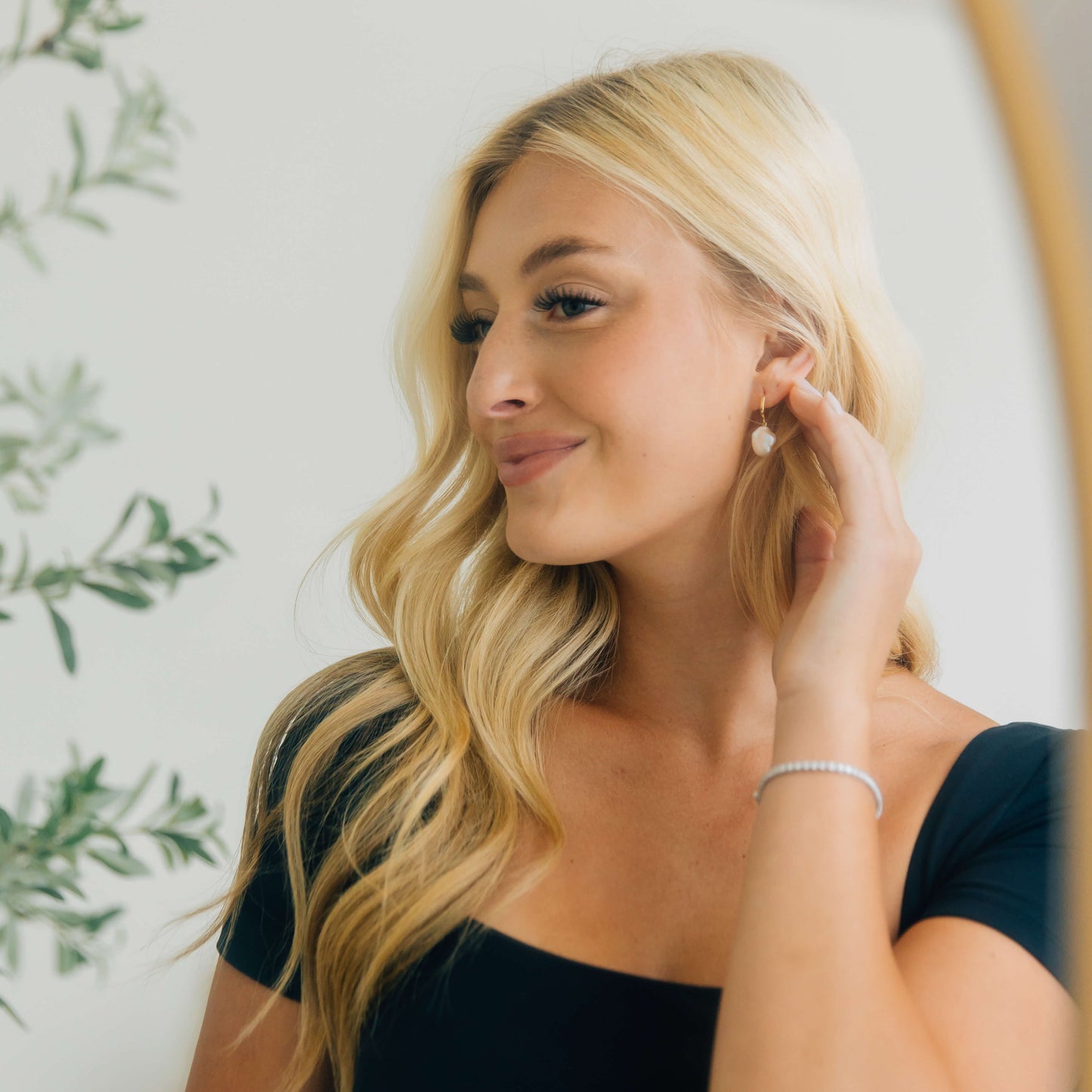 Woman adjusting earrings in front of a mirror with a blurred background