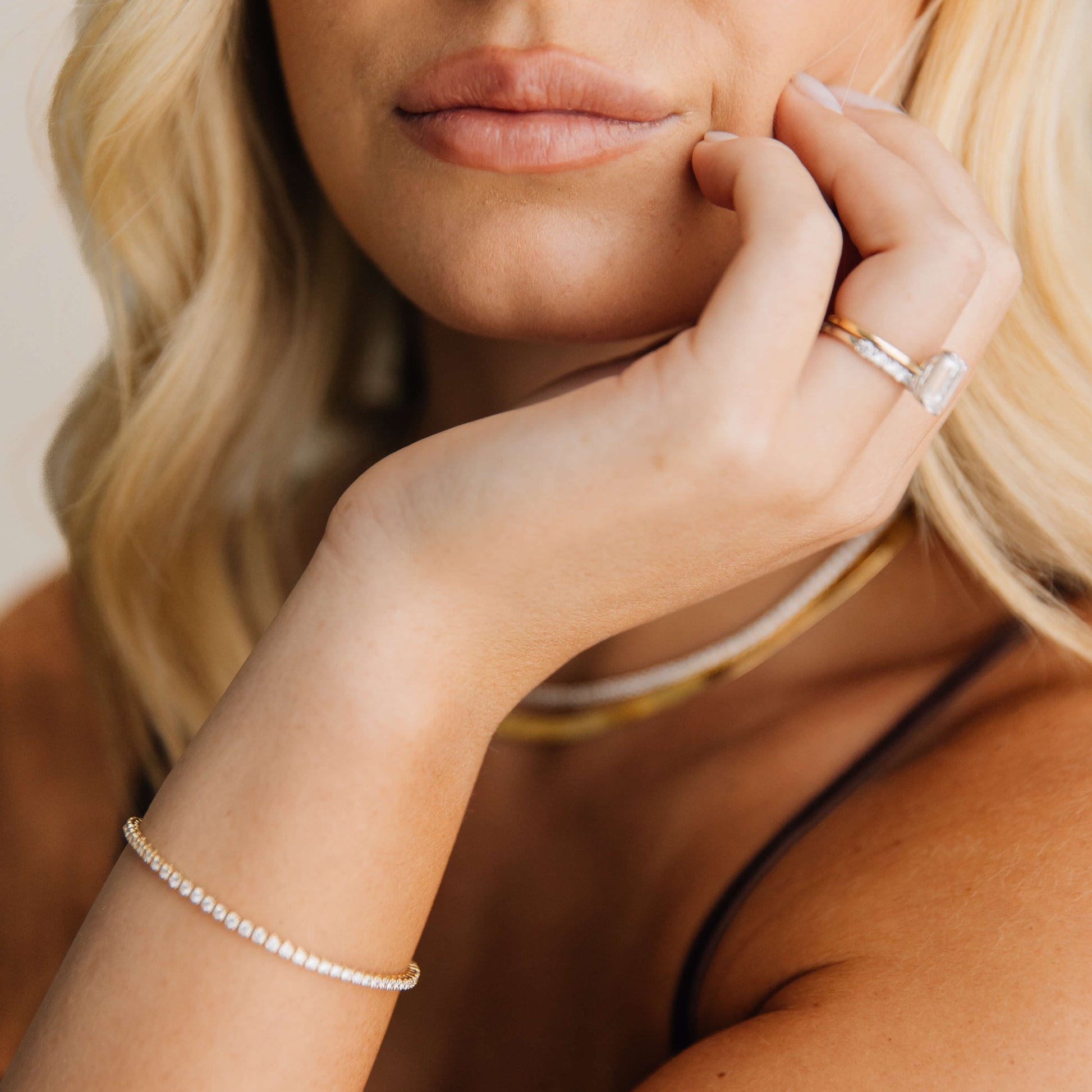 Close-up of a woman's face with blonde hair and jewelry, including a diamond ring and  14k yellow gold tennis bracelet.