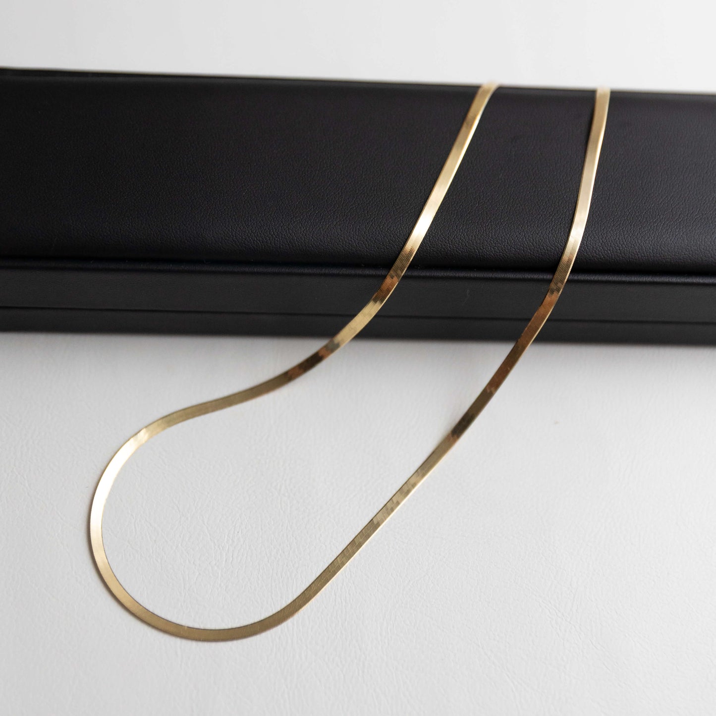 Gold herringbone necklace on a black stand against a white background