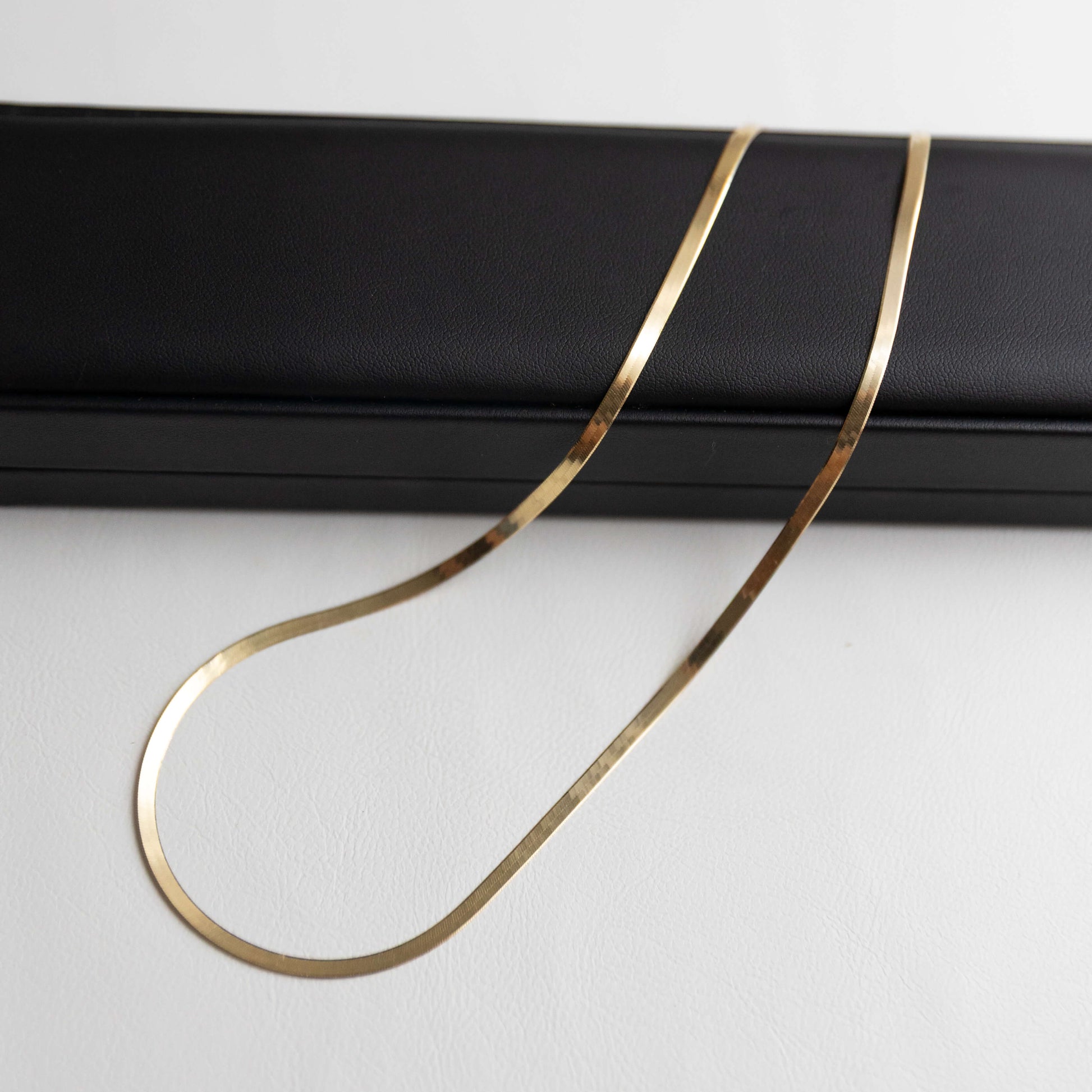 Gold herringbone necklace on a black stand against a white background
