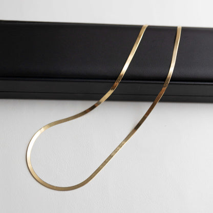 Gold herringbone necklace on a black stand against a white background