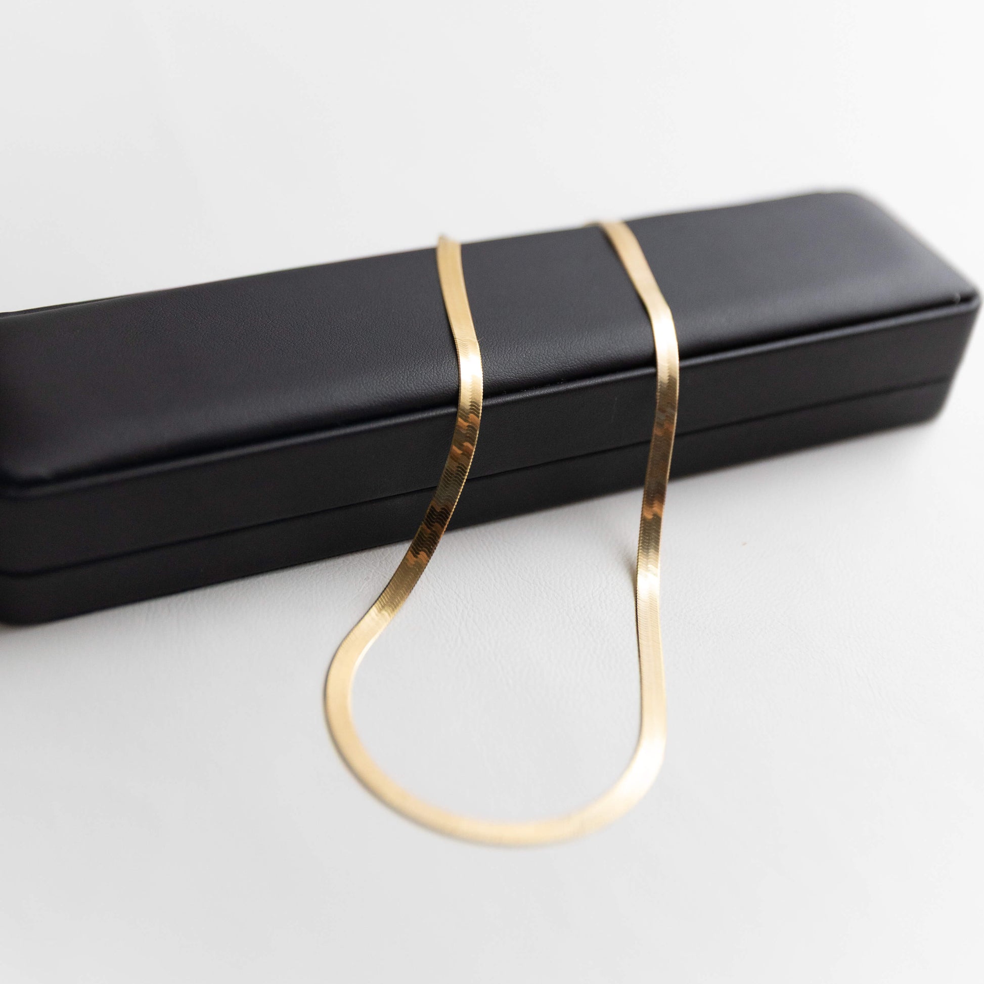 Gold herringbone necklace on a black jewelry box against a white background