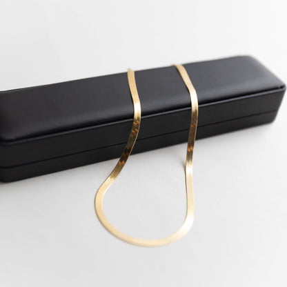 Gold herringbone necklace on a black jewelry box against a white background