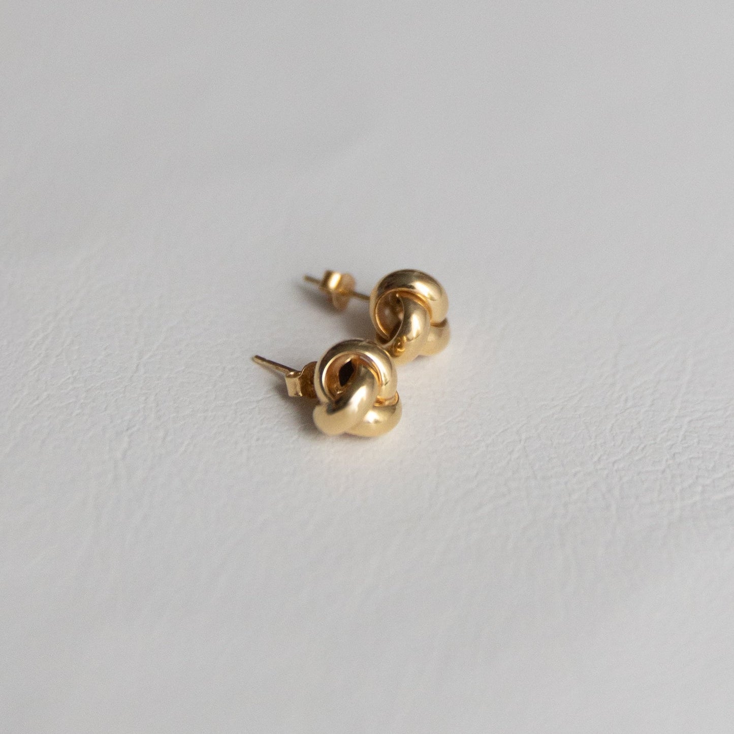 14K Gold love knot earrings on a light gray background