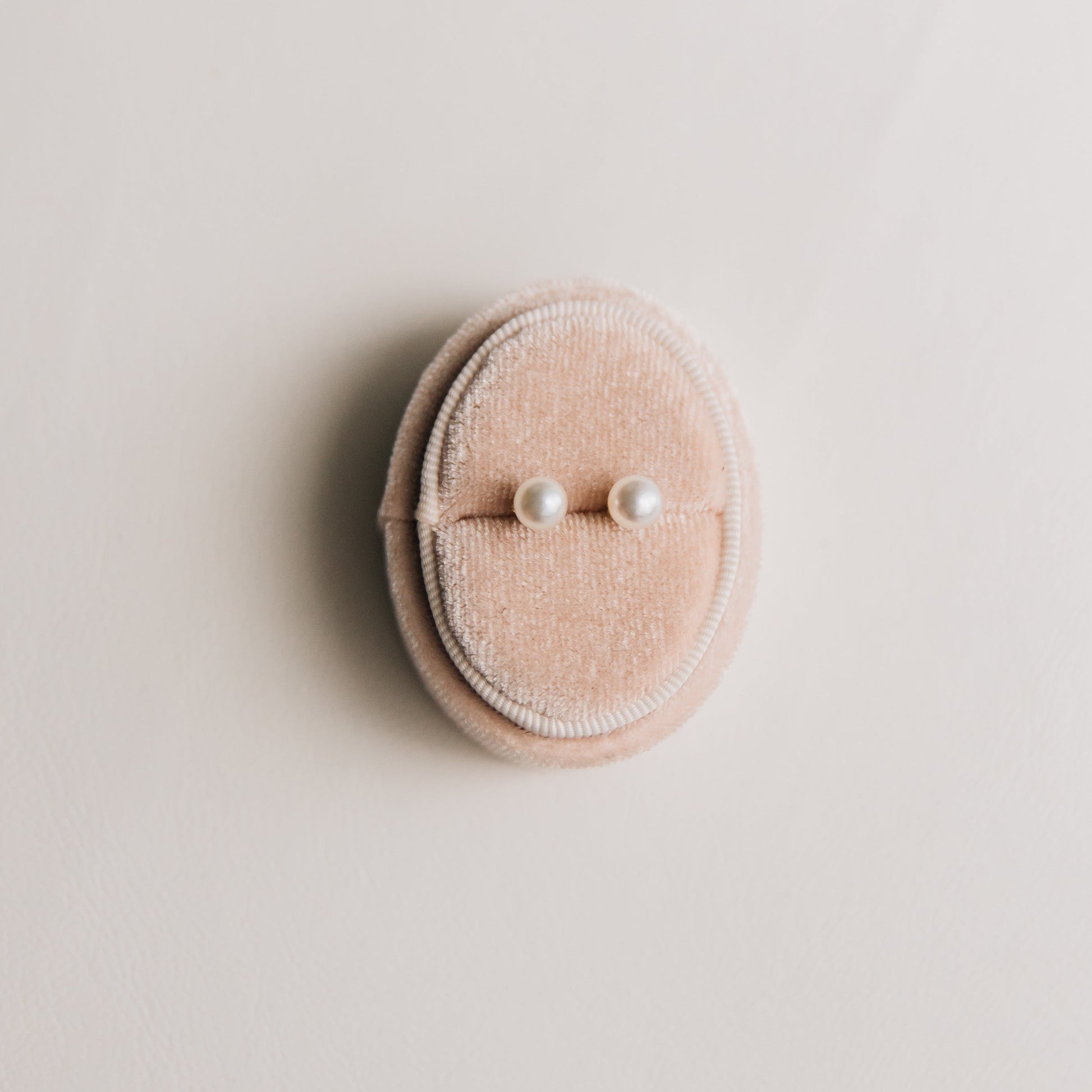 Pink velvet ring box with two pearl earrings on a light beige background