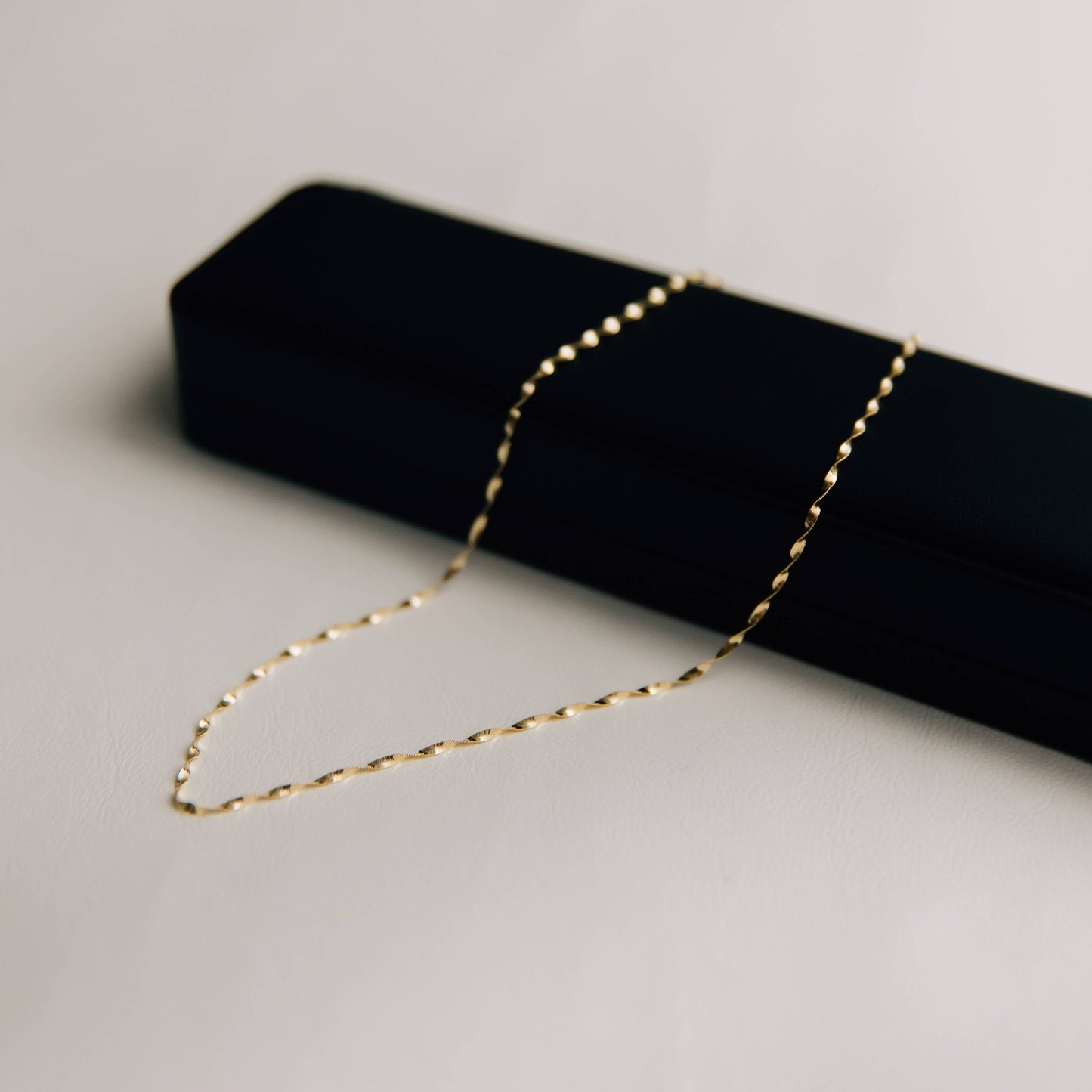 Gold twisted herringbone necklace on a black jewelry box against a light gray background