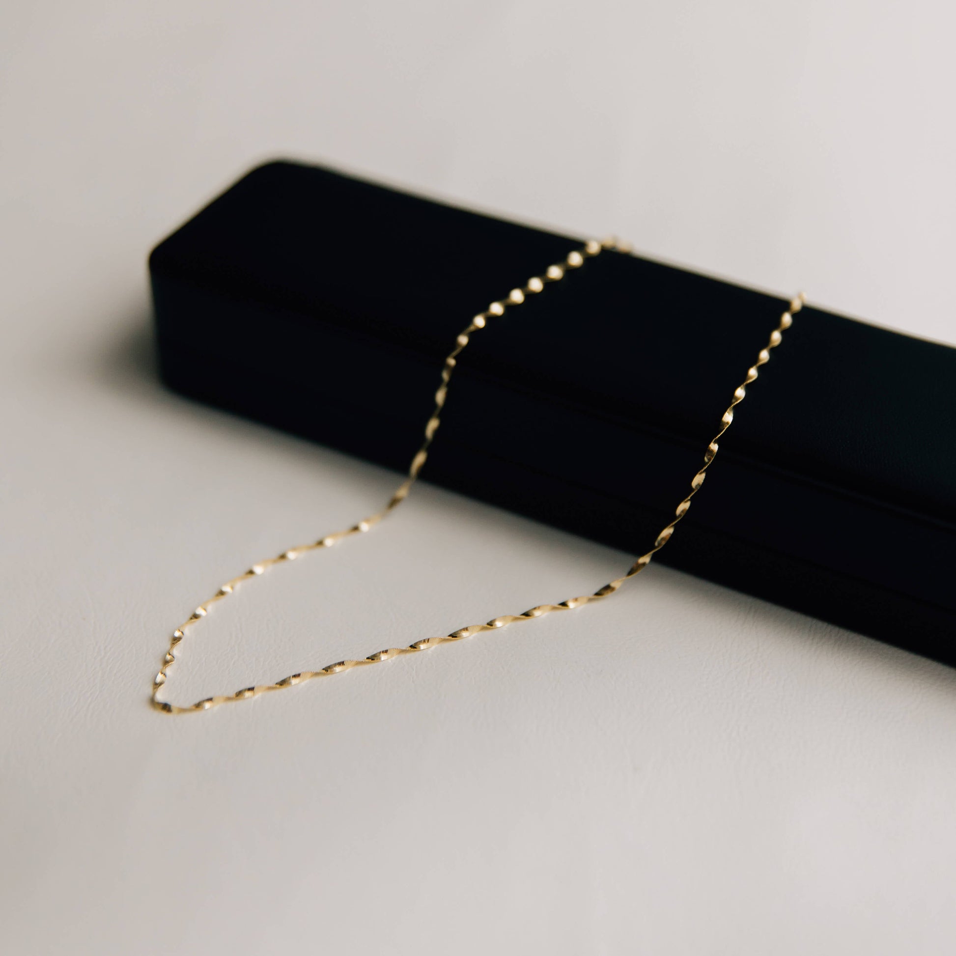 Gold twisted herringbone necklace on a black jewelry box against a light gray background