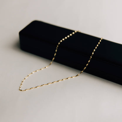Gold twisted herringbone necklace on a black jewelry box against a light gray background