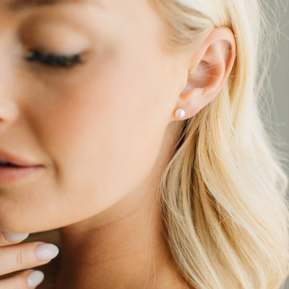 Close-up of a woman wearing a classic pearl stud earring.