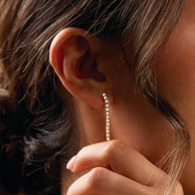 woman holding dangling diamond drop earrings in 14k white gold on a close up of her ear.