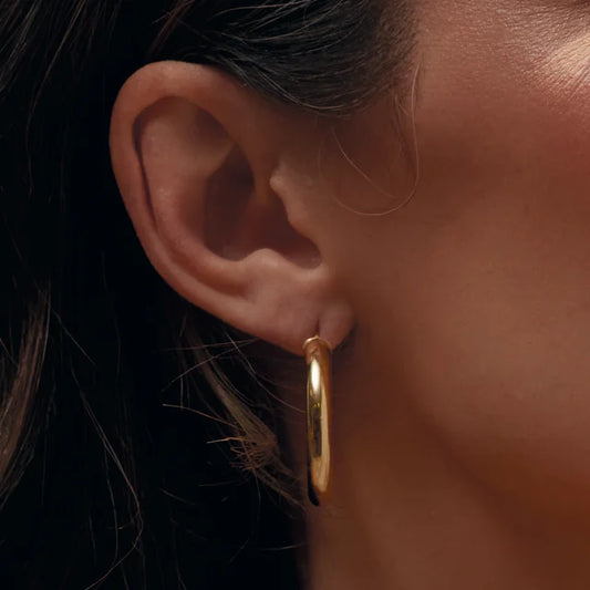 Thick gold hoops in 14k yellow gold close upon a woman's ear and face.