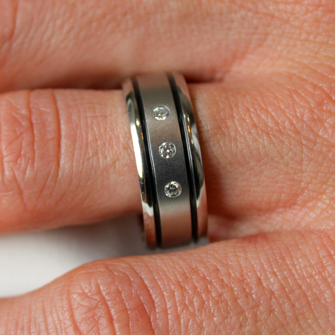 Cobalt chrome mens band with 3 lab grown diamonds and a two black inlays on a man's hand.