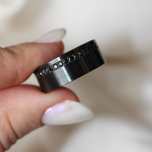Black zirconium men's wedding band with black lab grown diamonds and a ribbed finish on a white background.