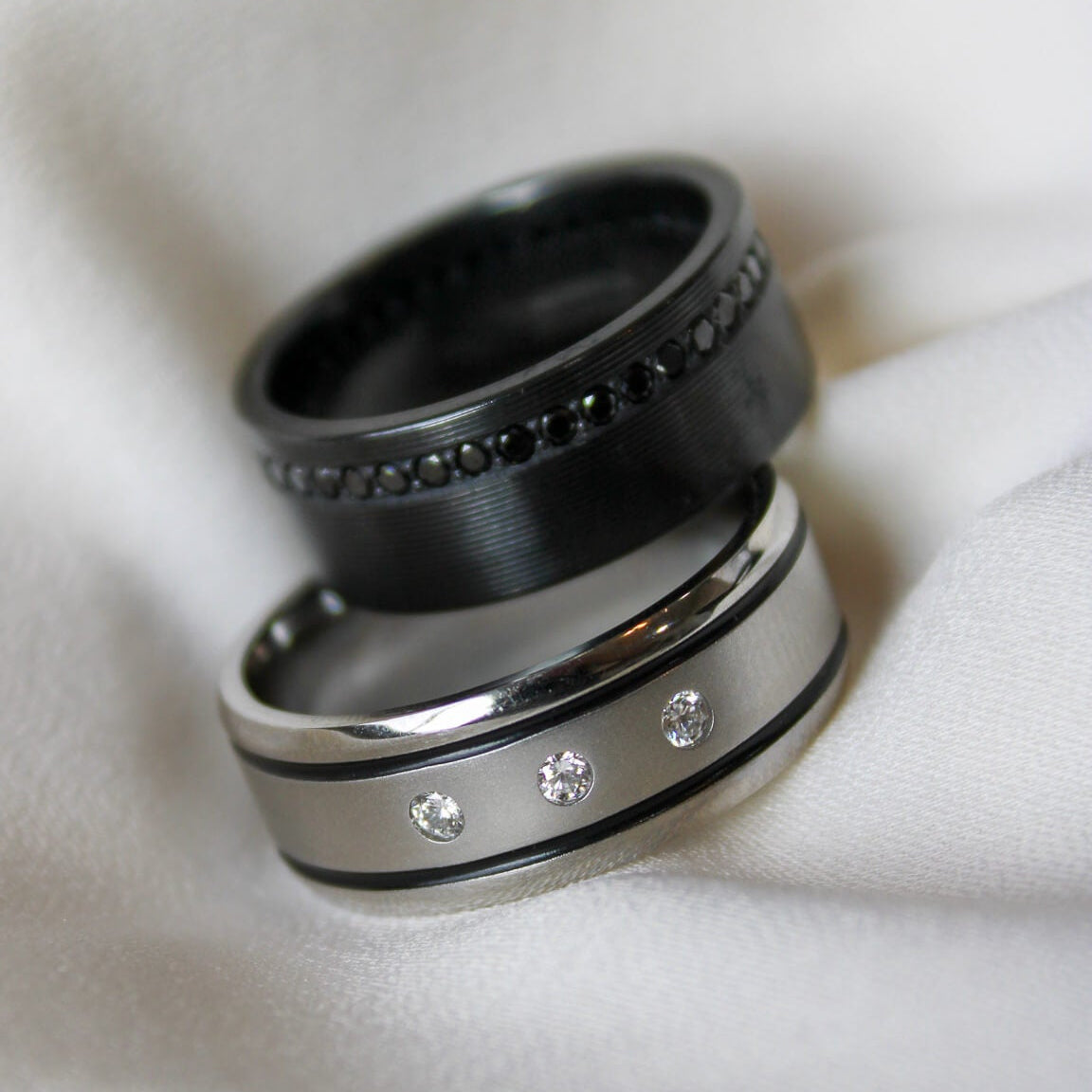 Cobalt chrome mens band with 3 lab grown diamonds and a two black inlays and a black zirconium ring with black lab grown diamonds on a white background.